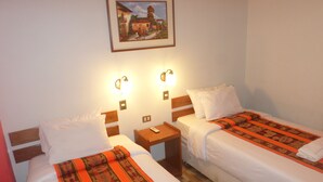 A hotel room with two beds, each with white linens and a patterned blanket. There are two bedside tables with lamps, a framed picture on the wall, and a wooden floor. - Hatun Pueblo Inn (Machu Picchu)