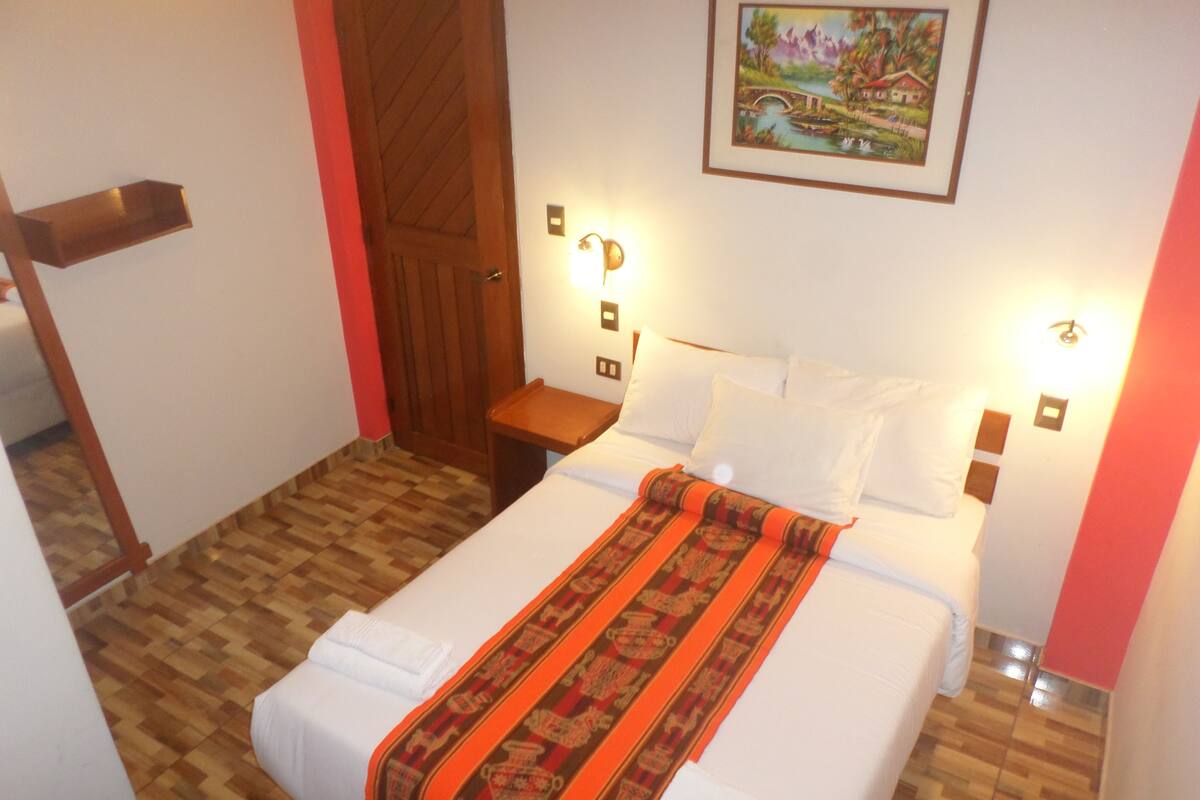 A neatly made bed with a patterned blanket, a wooden nightstand, and a wall-mounted light fixture.
