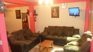 A living room with a brown sofa set, a wooden coffee table, and a television on the wall. - Hatun Pueblo Inn (Machu Picchu)