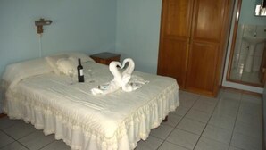 A neatly made bed with a bottle and glasses, a wooden wardrobe, and a small bedside table. - Hotel Salinas (Puerto Ayora)