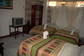 Una habitación de hotel con dos camas, un televisor sobre una mesita y un cuadro en la pared.