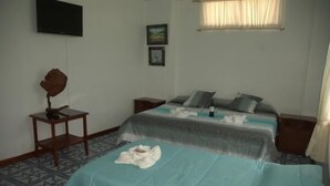A hotel room with a bed, a bedside table, a TV mounted on the wall, and a window with curtains. - Hotel Salinas (Puerto Ayora)