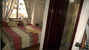 A bedroom with a bed, a wooden door, and a window with curtains. - Hotel Salinas (Puerto Ayora)