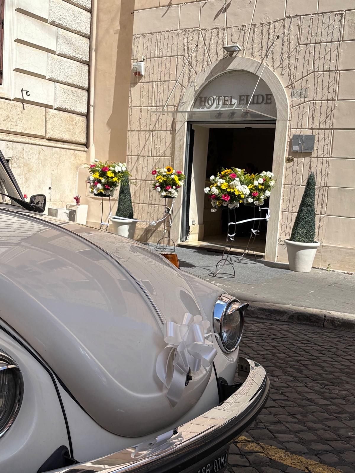 Un coche antiguo estacionado frente a la entrada de un hotel con un amplio arco y arreglos florales.