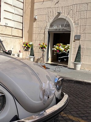 Un'auto d'epoca parcheggiata di fronte all'ingresso di un hotel, con un'ampia porta ad arco e composizioni floreali.