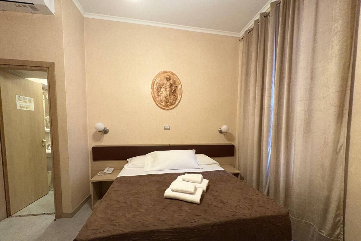 Una habitación de hotel con una cama, una obra de arte en la pared, una mesita de noche y una puerta.