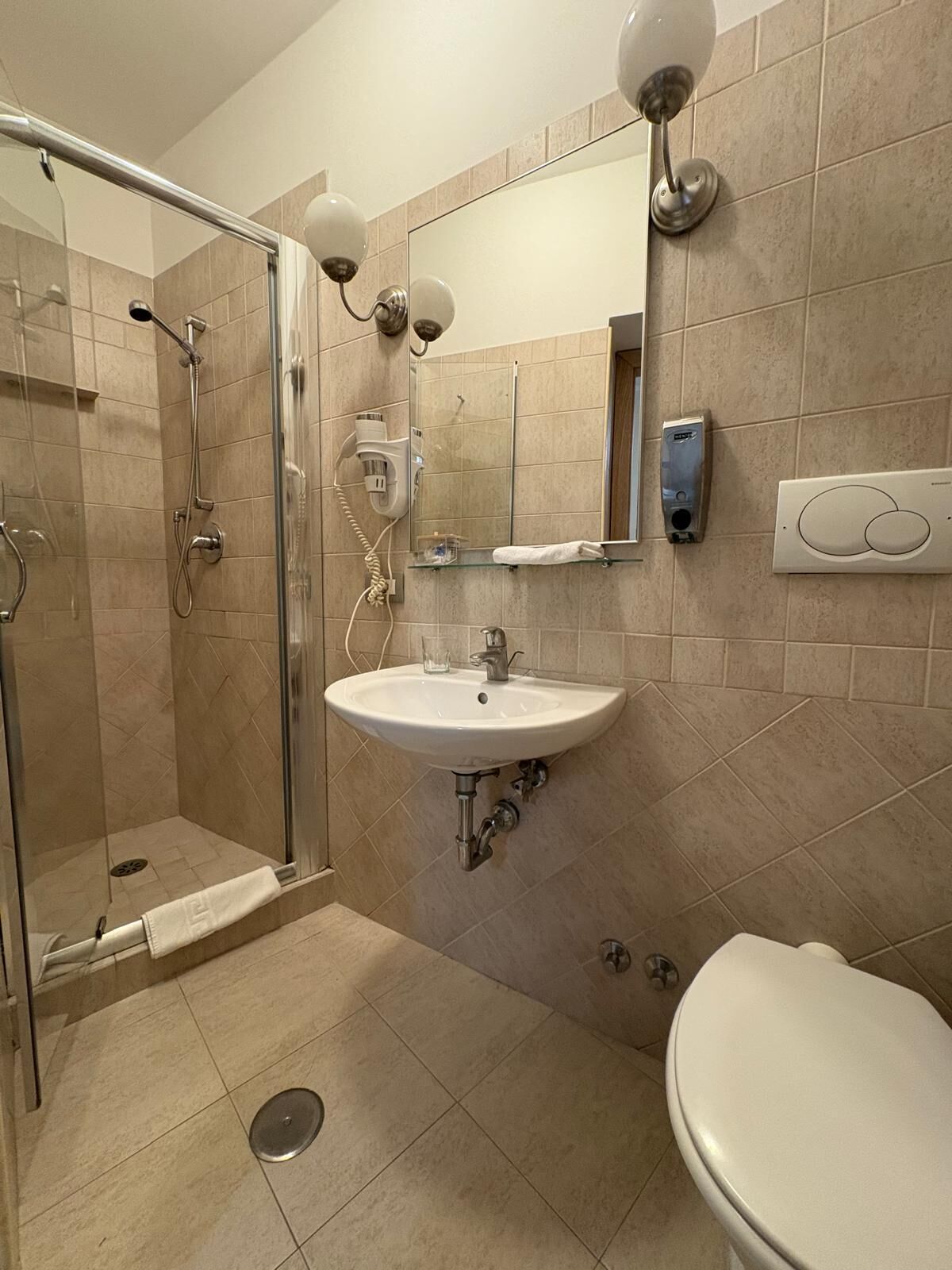 Un baño con cabina de ducha de vidrio, lavamanos, inodoro y espejo con luces empotradas.