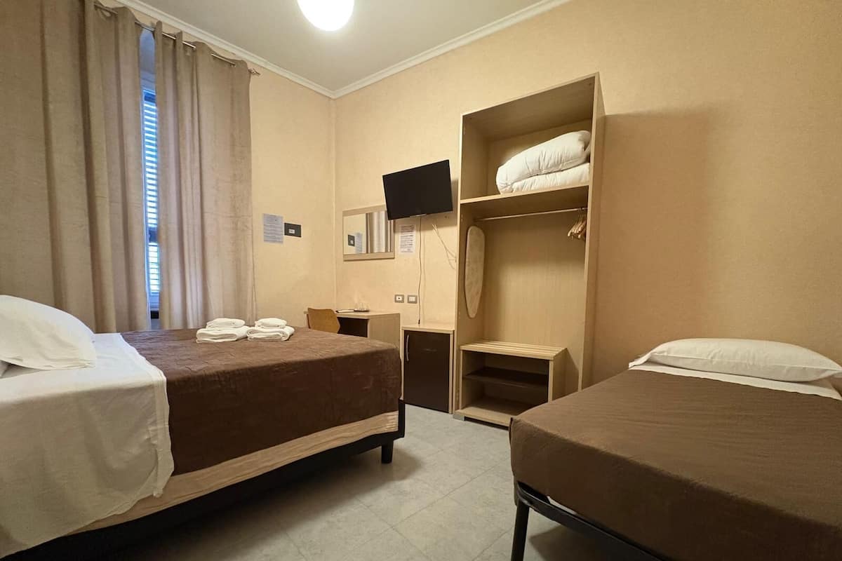 Habitación de hotel con dos camas, un escritorio, un televisor y un armario.