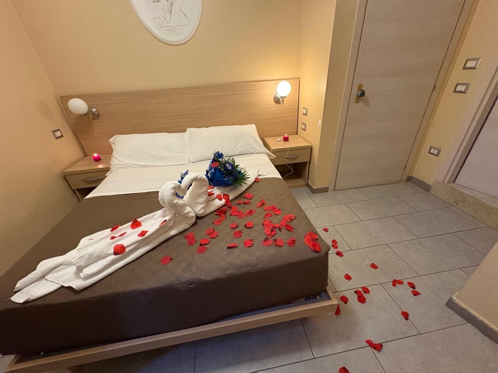 Una habitación de hotel con cama, mesita de noche, reloj de pared y puerta.
