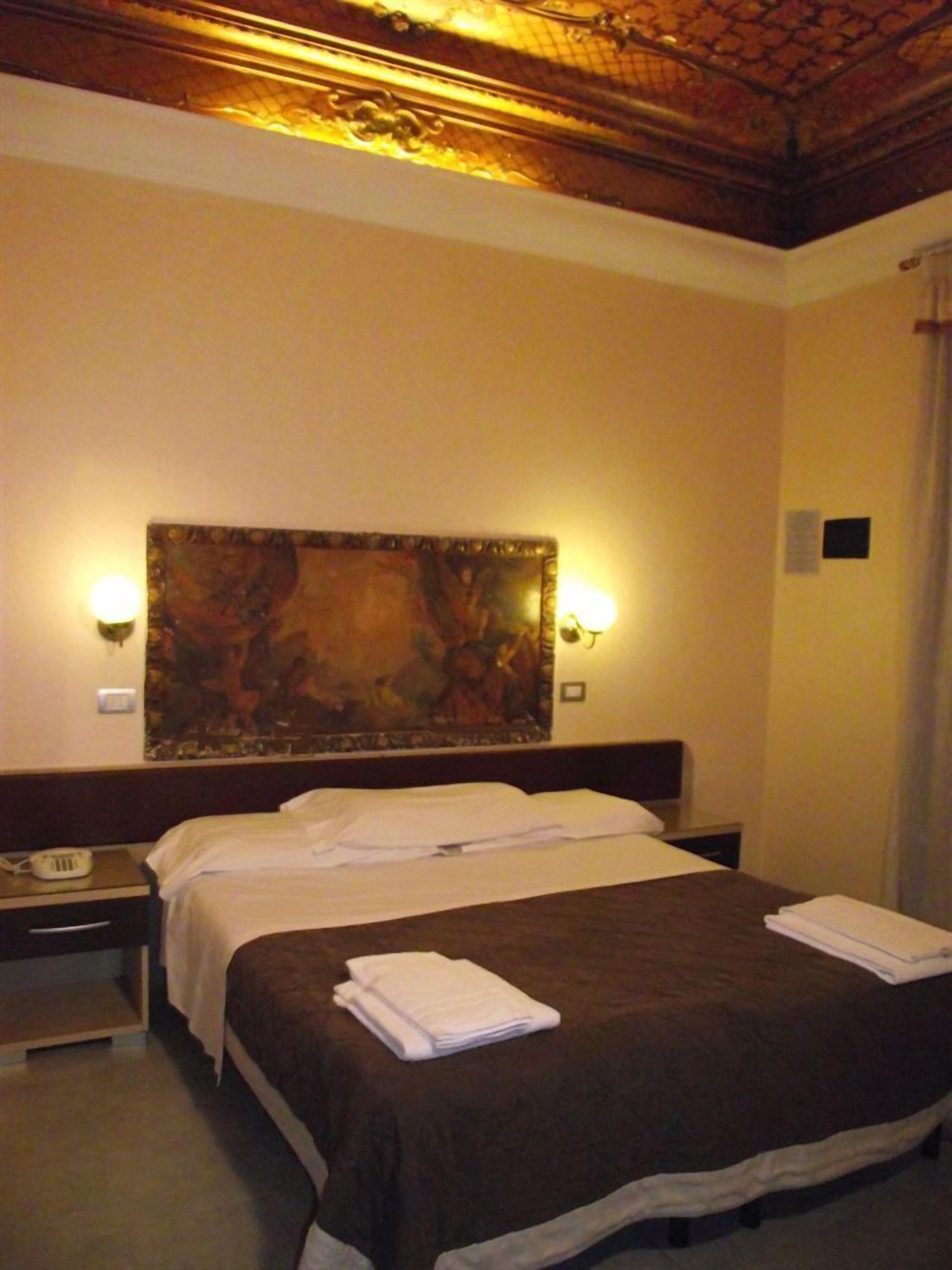 Habitación de hotel con una cama grande, dos lámparas de noche, un cuadro en la pared y un teléfono en la mesita.
