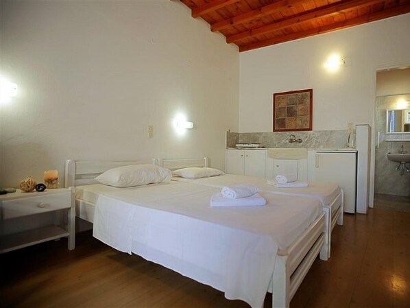 Un dormitorio con dos camas, una mesita de noche, una pequeña mesa y un baño con lavabo y espejo.