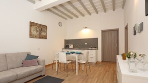 Una sala de estar moderna con sofá, mesa de comedor y sillas. Se observa un área de cocina al fondo, con microondas y fregadero.