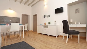 Una cocina moderna con salpicadero de azulejos, una zona de comedor con sillas blancas, una consola blanca y una silla negra.