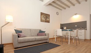 A modern living room with a sofa, a dining table with chairs, a kitchen area with a microwave, and a clock on the wall. - Belsiana 7 Central (Rome)