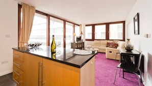 Cozinha moderna com ilha central, área de jantar com mesa e cadeiras, e sala de estar com sofá e mesa de centro.