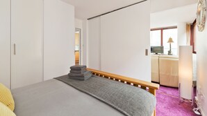 Um quarto moderno com uma cama, um banco de madeira, um espelho e uma janela.