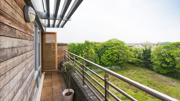 A balcony with wooden walls, a metal railing, and a view of a green landscape. - Birch at Inchicore (Dublin)