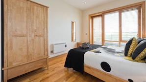 A bedroom with a wooden wardrobe, a bed with a polka dot bedspread, and a window with blinds. - Birch at Inchicore (Dublin)