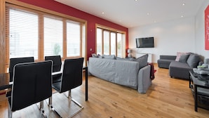 A modern living room with a grey sofa, a dining area with black chairs, and a flat-screen TV mounted on the wall. - Birch at Inchicore (Dublin)