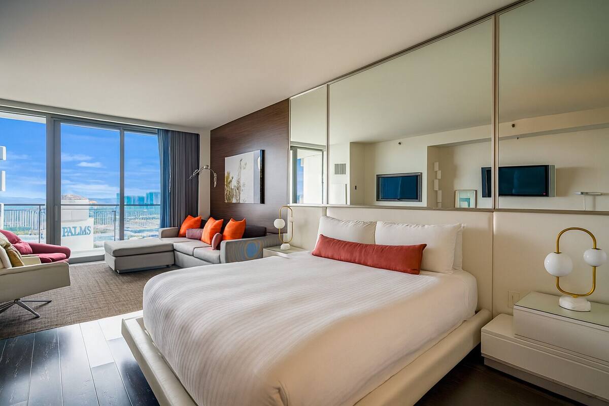 Une chambre d’hôtel moderne, dotée d’un grand lit, d’un canapé, d’un bureau et d’une télévision. La chambre dispose de grandes fenêtres et offre une vue sur la ville.