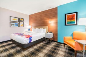 A hotel room with a bed, a nightstand, a chair, a lamp, and a wall with framed pictures.