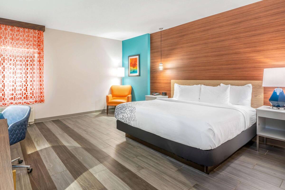A hotel room with a large bed, a desk, a chair, and a window with patterned curtains.