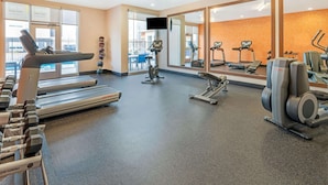 Une salle de sport équipée de tapis de course, d’appareils de musculation et d’un mur entièrement recouvert de miroirs.