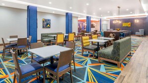 Un hall d’hôtel doté de plusieurs espaces de détente, comprenant des tables et des banquettes, ainsi qu’un comptoir central.