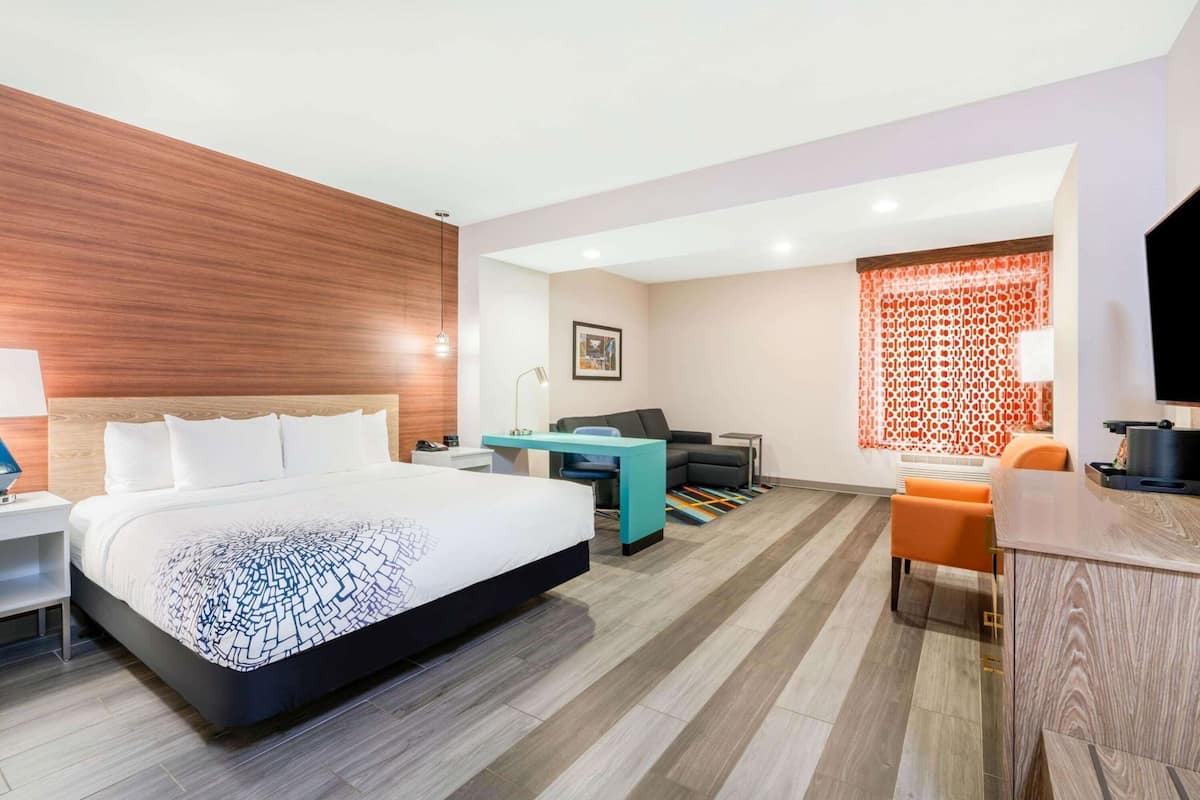 A modern hotel room with a large bed, a desk, a sofa, and a TV.