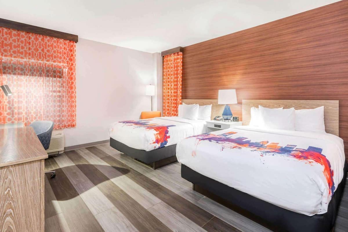 A hotel room with two beds, a desk, and a chair.