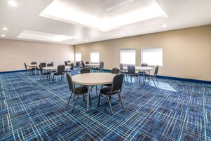 Un salón de conferencias con mesas y sillas redondas, ventanas amplias y una alfombra estampada.