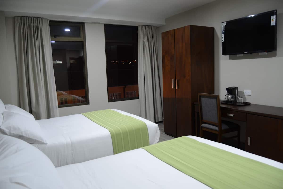Una habitación de hotel con dos camas, un escritorio, una silla, un televisor y un armario.