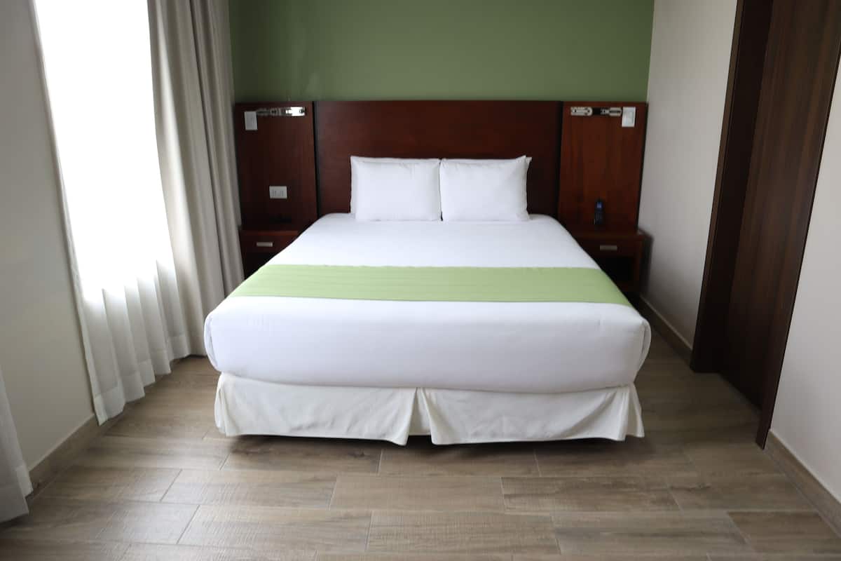 Una habitación de hotel con una cama grande, cabecero de madera, ropa de cama blanca y un detalle en verde.