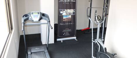 Zona de gimnasio con cinta de correr, elíptica y máquina de pesas.