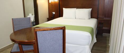 A hotel room with a bed, a nightstand, a table with two chairs, and a mirror.