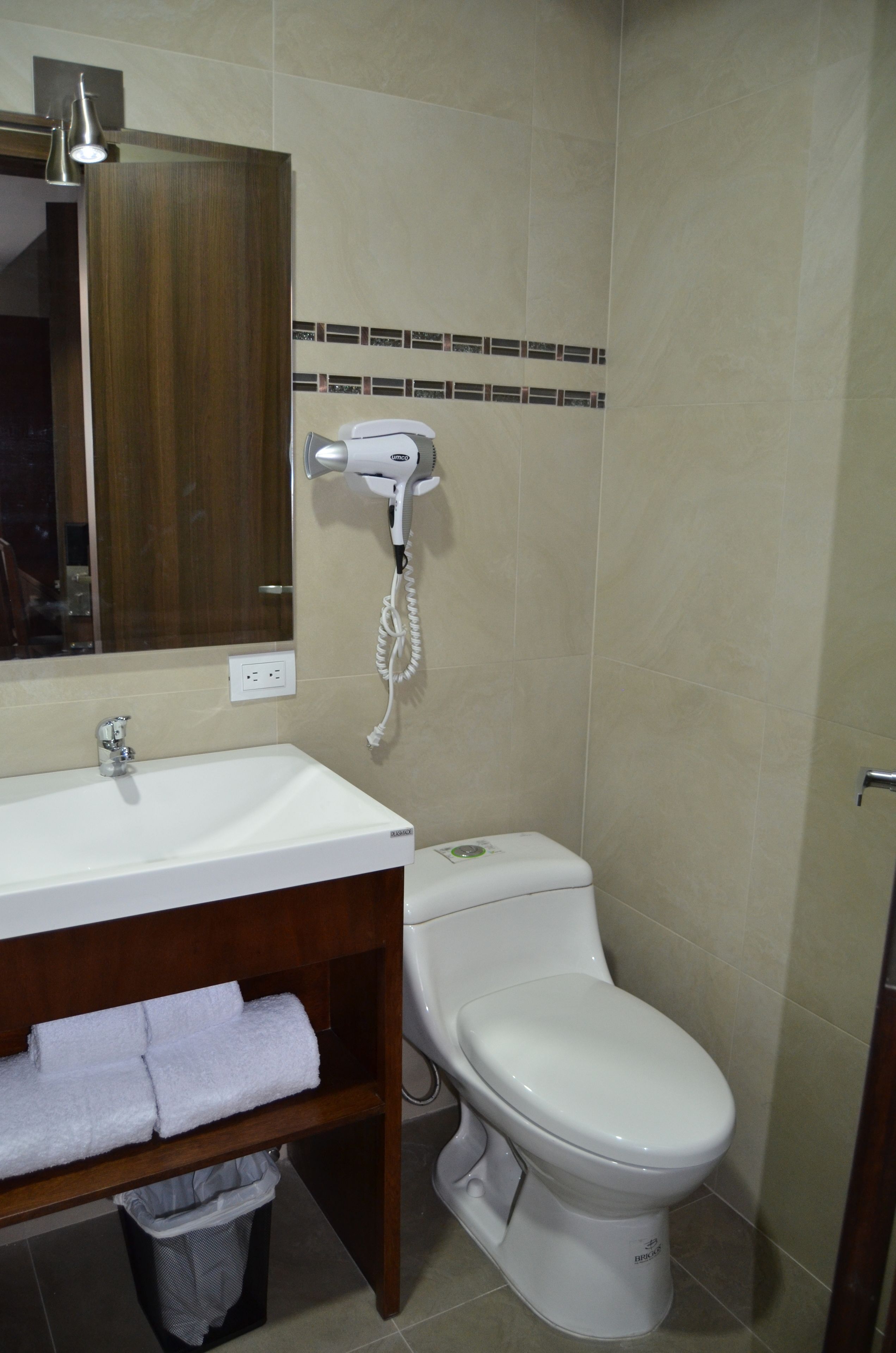 Un baño con un lavabo blanco, un espejo, un secador de pelo y un inodoro.