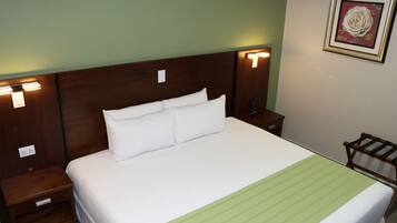 Una cama bien tendida con sábanas blancas y una colcha a rayas verdes, flanqueada por mesitas de noche de madera con lámparas fijadas a la pared.