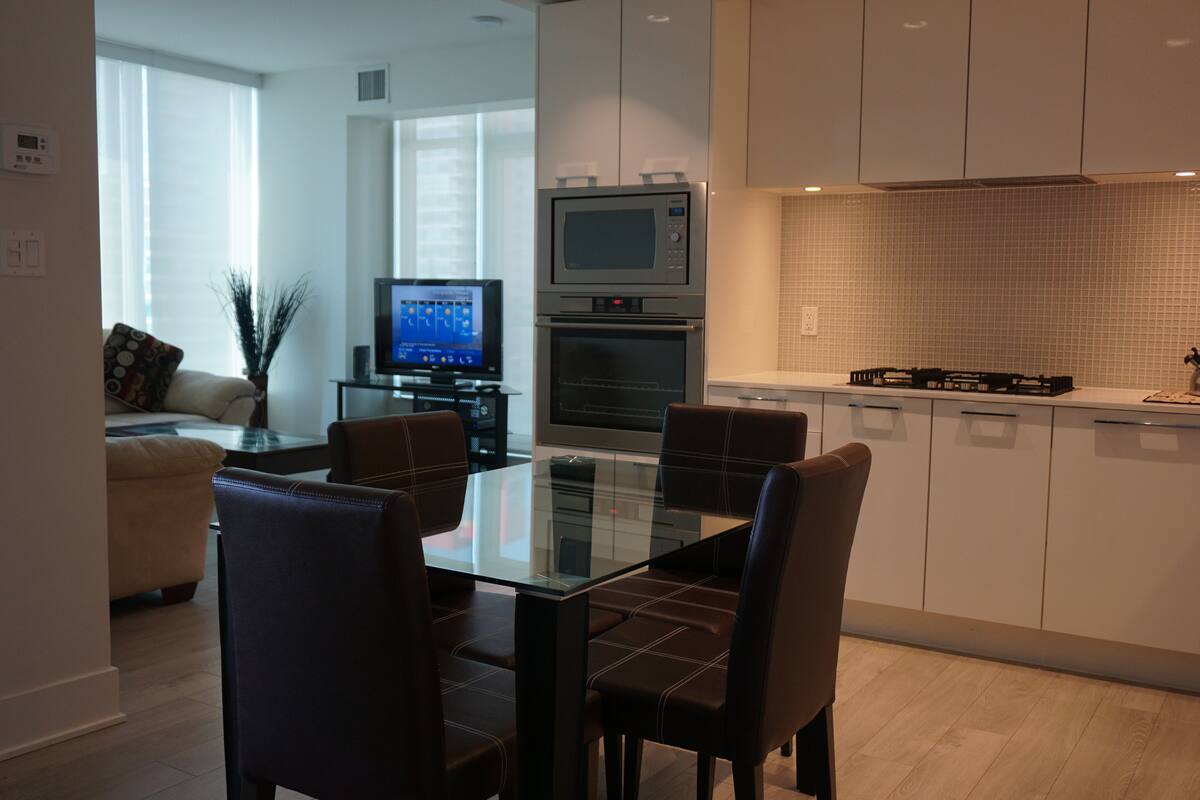 A modern kitchen with white cabinets, a glass dining table, and a built-in oven.