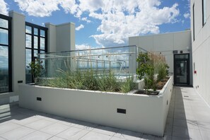 Un espacio exterior moderno con barandilla de vidrio, jardineras blancas con plantas y una vista despejada del cielo.