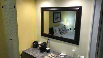 A hotel bathroom with a granite countertop, a coffee maker, a bottle of hand soap, and a glass of water.