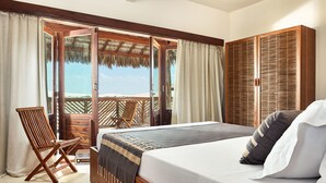 A room with a bed, wooden chair, and a view of the beach. - Villa Majica (Jijoca de Jericoacoara)