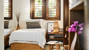 A bedroom with two beds, a bedside table with books and a lamp, and a window with a view of greenery. - Villa Majica (Jijoca de Jericoacoara)