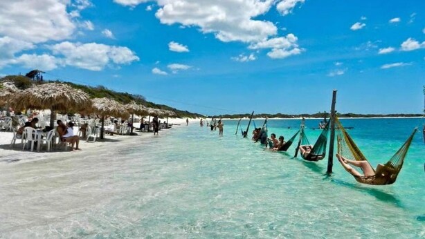A beach with clear turquoise water, people relaxing in hammocks, and a dining area with tables and umbrellas. - Villa Majica (Jijoca de Jericoacoara)