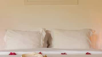 A bed with white linens, a framed picture on the wall, and scattered rose petals.