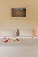 A bed with white linens, a framed picture on the wall, and scattered rose petals.
