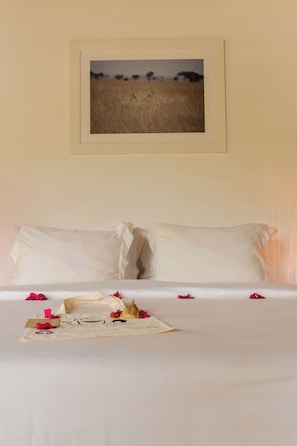 Una cama con sábanas blancas, un cuadro en la pared y pétalos de rosa esparcidos.