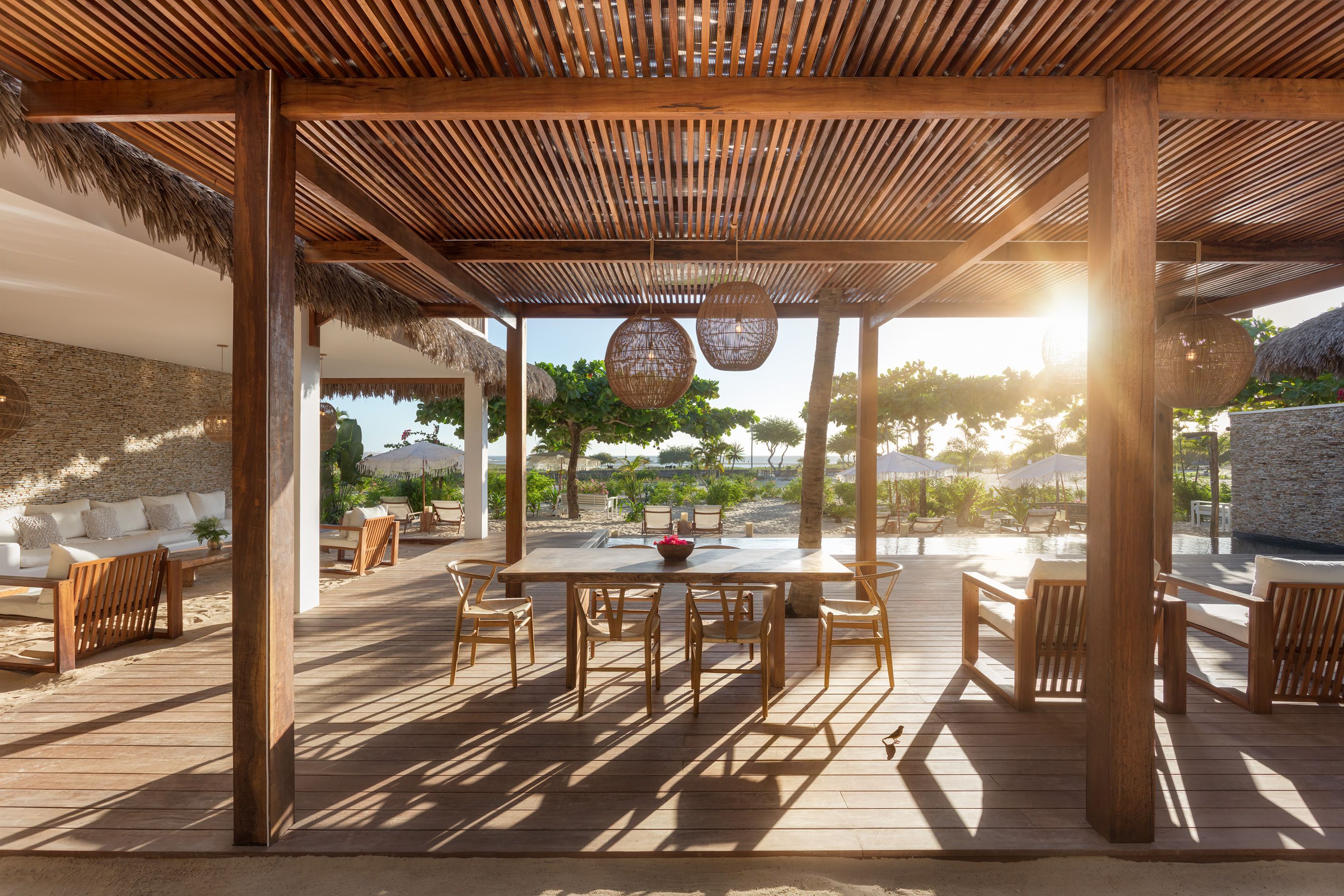 Una terraza de madera al aire libre con un pérgola, zona de estar y vista a la playa.