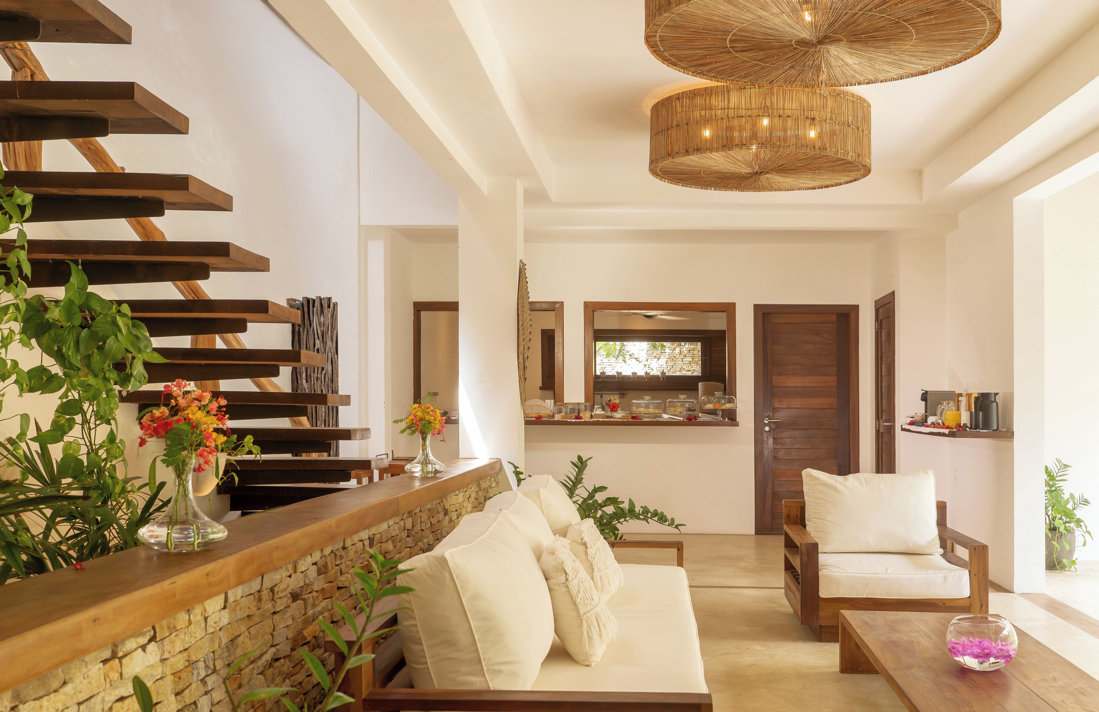 Una sala de estar moderna con pared de piedra, escalera de madera y comedor con cocina al fondo.