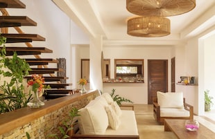 A modern living room with a stone wall, wooden staircase, and a dining area with a kitchen in the background.