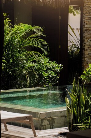 Uma área de piscina com espreguiçadeira, rodeada por vegetação exuberante e um muro de pedra.